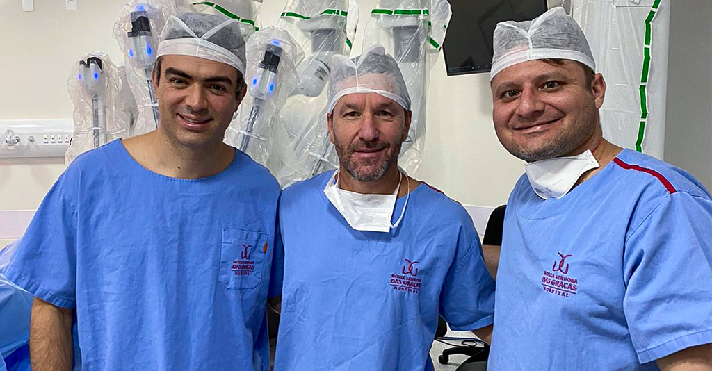 Fotografia da equipe da equipe de cirurgiões do Dr. André Berger no Hospital Nossa Senha das Graças. No fundo o Robô da Vinci Xi
